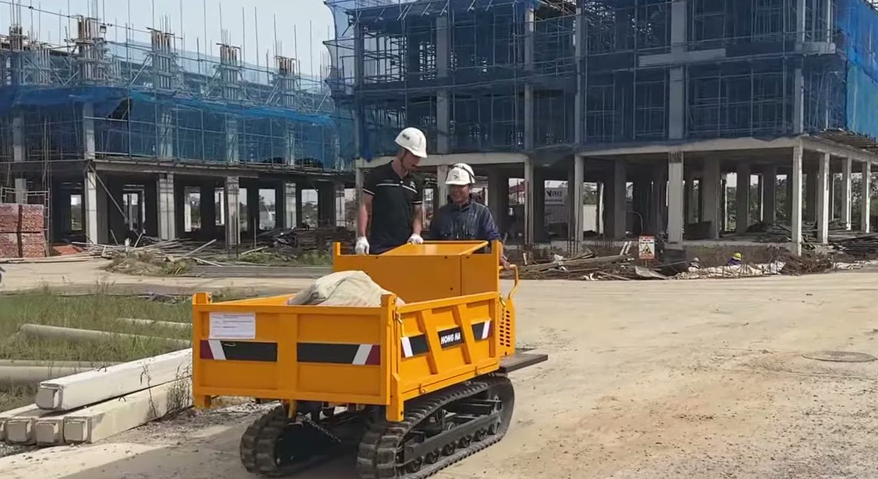 Xe rùa bánh xích 1,8 tấn chở bao vật liệu trước dãy nhà đang xây