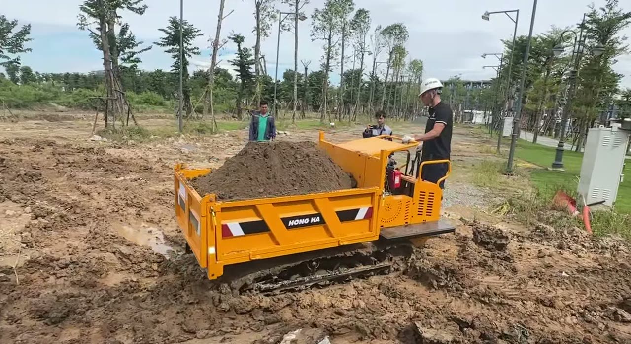 Xe rùa bánh xích 1,8 tấn chở đầy thùng đất giữa các hàng cây