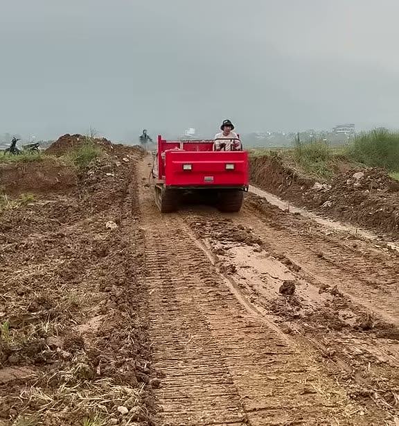 Xe rùa bánh xích chở vật liệu trên đường đất giữa cánh đồng Thạch Thất
